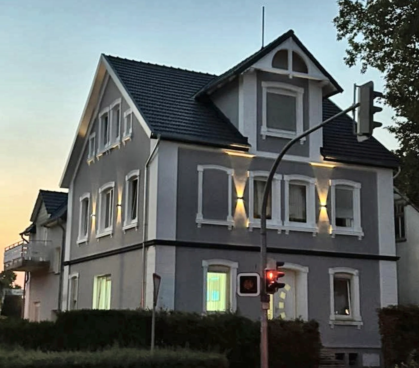 Nachher: dieselbe Fassade in Anthrazit mit weißen Fensterfaschen, dunklem Dach und warmer Fassadenbeleuchtung in der Abenddämmerung